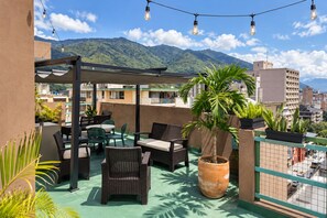 Une terrasse sur le toit, aménagée avec du mobilier d’extérieur, un pot de fleurs et offrant une vue sur un paysage montagneux.