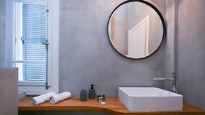 Un baño con lavamanos blanco, un espejo redondo y una ventana con persianas.