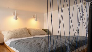 A bed with a grey blanket, two pillows, and a wooden frame. There are two wall-mounted lamps on either side of the bed. - Red Brick Apartament w Rynku ProperUNIT (Wroclaw)