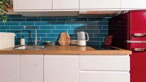 A kitchen with white cabinets, a blue tiled backsplash, a red refrigerator, and a wooden cutting board. - Red Brick Apartament w Rynku ProperUNIT (Wroclaw)