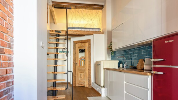 A kitchen with white cabinets, a red refrigerator, and a wooden staircase leading to a loft area. - Red Brick Apartament w Rynku ProperUNIT (Wroclaw)