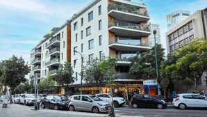 Un edifici de diversos pisos amb balcons, cotxes aparcats i un local comercial amb cartell electrificat.