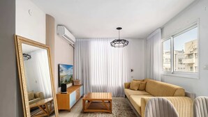 Una sala de estar moderna con un sofá, una mesa de centro de madera, un espejo grande y un televisor sobre un mueble de madera.