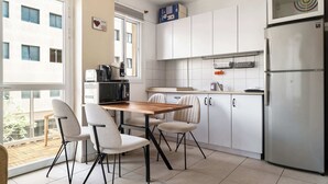 Una cocina moderna con alacenas blancas, un refrigerador de acero inoxidable y un comedor con mesa y sillas de madera.