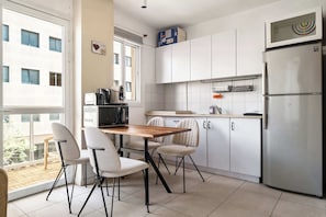 A modern kitchen with white cabinets, a stainless steel refrigerator, and a dining area with a wooden table and chairs.