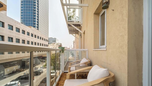 Un balcón con vista a una calle concurrida, una silla de madera y una mesita.