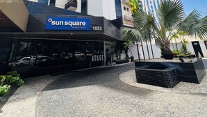 Un hôtel moderne, reconnaissable à son panneau bien visible indiquant « Sun Square Suites Hotel », doté d’un espace extérieur bien entretenu avec des palmiers et offrant une vue sur un ciel dégagé.