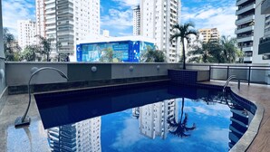 Une piscine sur le toit offrant une vue dégagée sur les immeubles environnants et un ciel bleu.