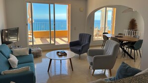Een ruime woonkamer met een grote schuifpui die uitkomt op een balkon met uitzicht op zee.