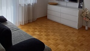 Un salon doté d’un téléviseur à écran plat, d’un meuble blanc, d’un canapé gris et d’un parquet en bois.