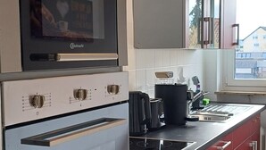 Une cuisine équipée d’un four encastré, d’une plaque de cuisson et de meubles de rangement rouges.