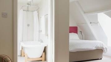Quarto com cama, banheiro com banheira e porta que dá para outro cômodo.
