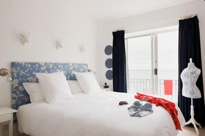 A hotel room with a large bed, a nightstand, a dresser, a window with curtains, and a balcony with a railing.