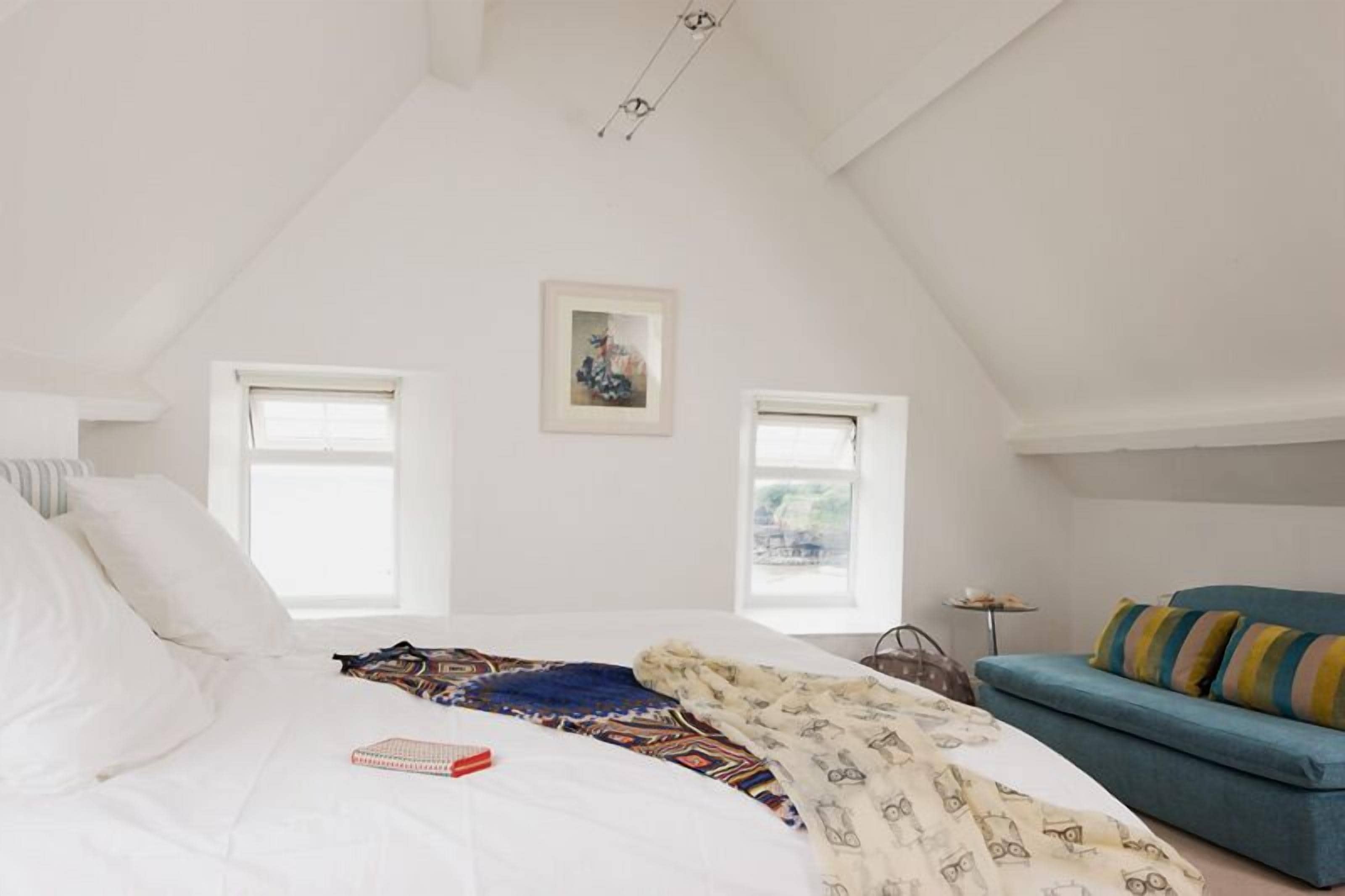 A bedroom with a bed, a blue sofa, two windows, and a framed picture on the wall.
