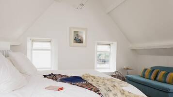 A bedroom with a bed, a blue sofa, two windows, and a framed picture on the wall.