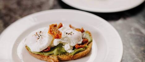Un plato de desayuno con huevos pochados, aguacate y tocino sobre tostada.