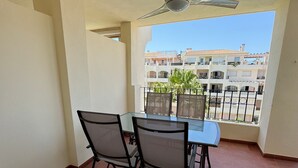 Un balcón con mesa y sillas, un ventilador de techo y vistas a edificios al fondo.