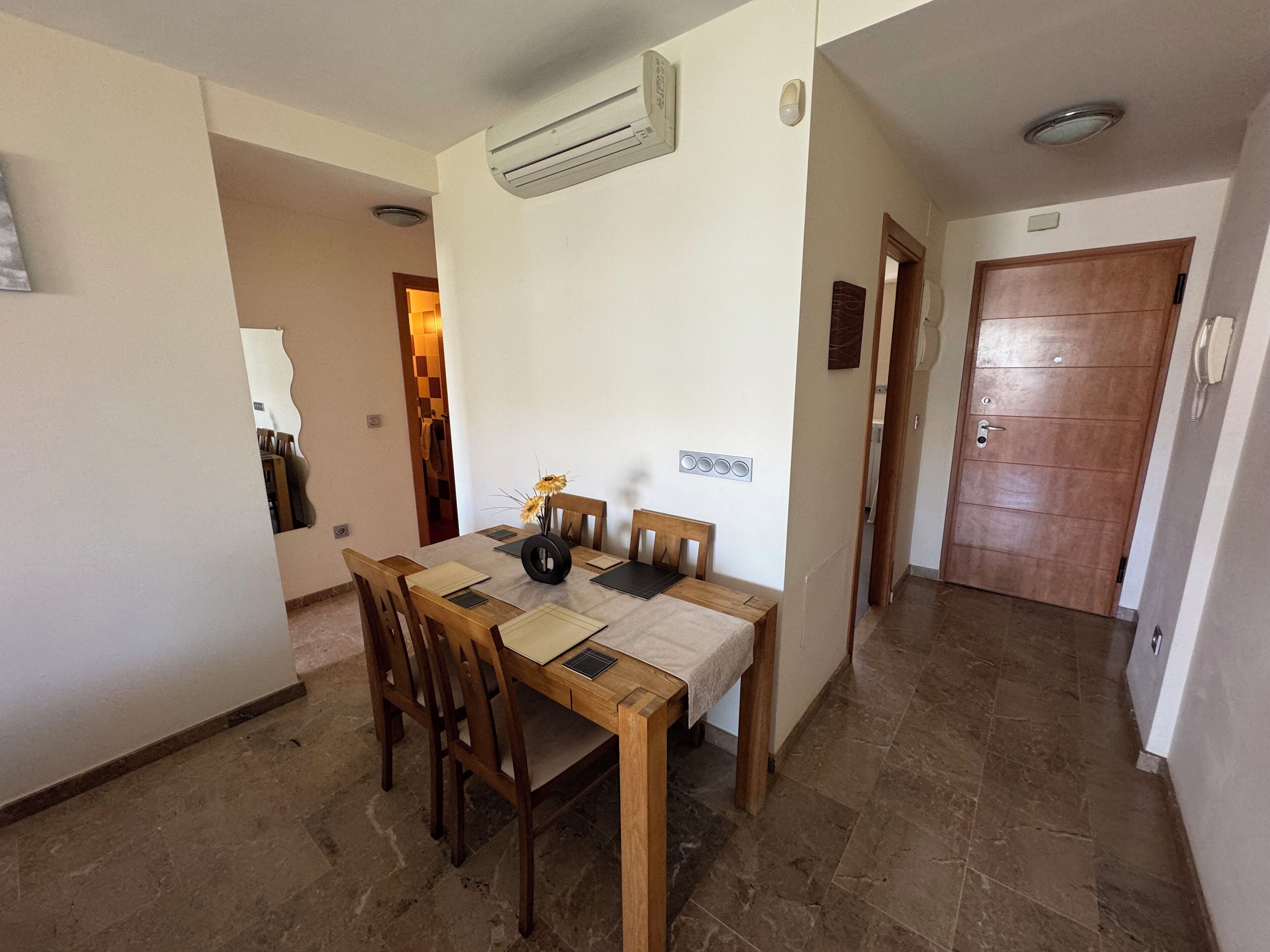 Un comedor con mesa y sillas de madera, un equipo de aire acondicionado y piso de baldosas.