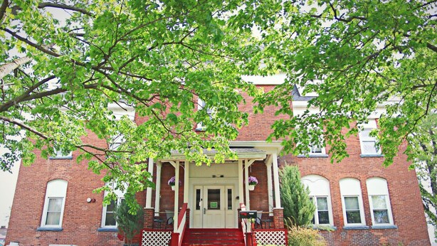 A brick building with a white porch, red steps, and a small garden area. - Foothills Lodge & Diner (Malone)