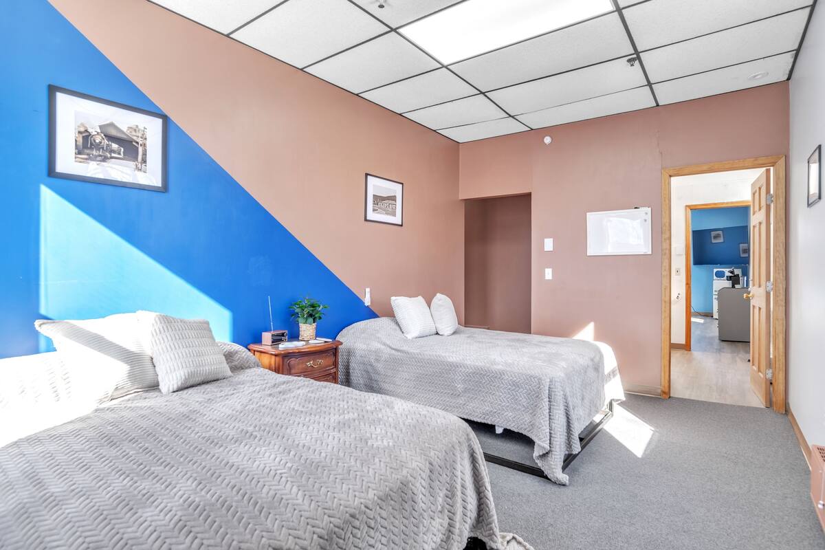 Habitación de hotel con dos camas, una mesita de noche de madera, una planta en maceta y un cuadro en la pared.
