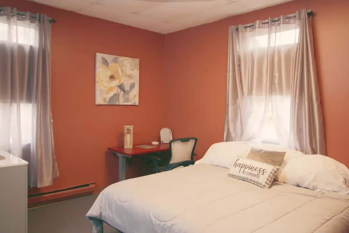 Un dormitorio con cama, escritorio, silla y un cuadro en la pared.