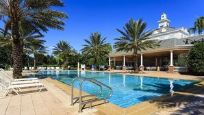 Una piscina con sillas de descanso y palmeras, rodeada por un edificio con una torre.
