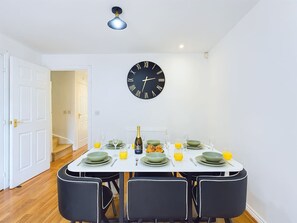 Ein Essbereich mit einer runden schwarzen Uhr an der Wand, einem Tisch mit Tellern, Gläsern und einer Champagnerflasche.