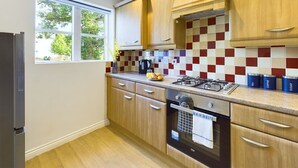 A modern kitchen with wooden cabinets, a tiled backsplash, a gas stove, and a built-in oven. - Spacious House | Parking | Business & Leisure (Gloucestershire)
