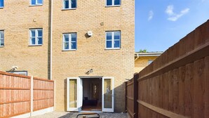 A courtyard with a table set for dining, a wooden fence, and a building entrance. - Spacious House | Parking | Business & Leisure (Gloucestershire)