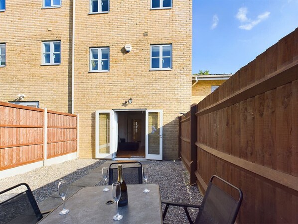 A courtyard with a table set for dining, a wooden fence, and a building entrance.