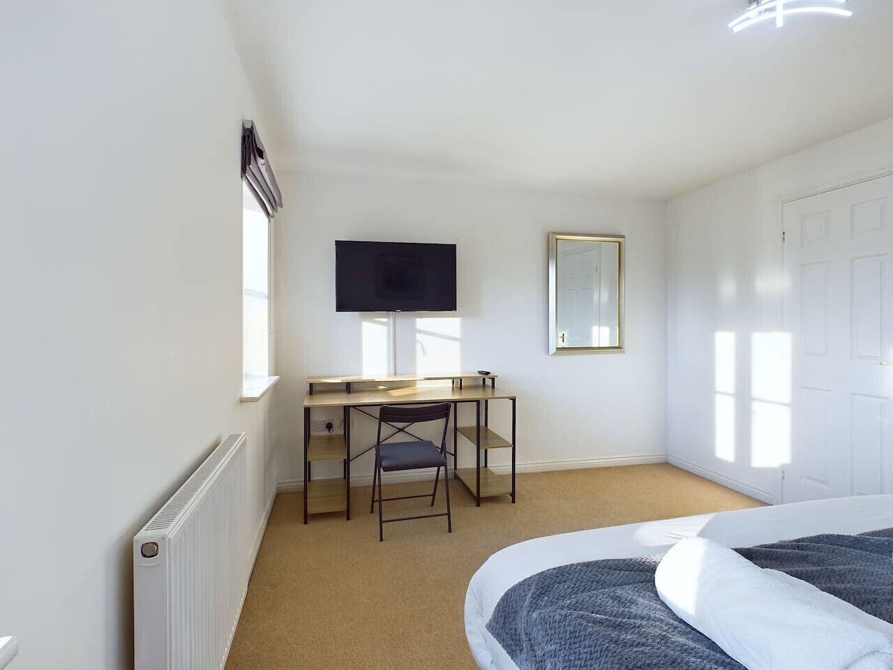 Ein Schlafzimmer mit Bett, Schreibtisch, Stuhl, Fernseher, Spiegel und Heizk örper.