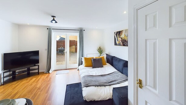 A bedroom with a bed, a television, and a sliding glass door leading to an outdoor area. - Spacious House | Parking | Business & Leisure (Gloucestershire)