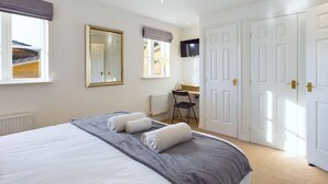 A bedroom with a bed, two rolled towels, a desk with a chair, a television, and a large mirror. - Spacious House | Parking | Business & Leisure (Gloucestershire)