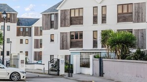 Un moderno edificio residencial de varios pisos con fachada blanca, contraventanas de madera y entrada protegida por una reja.