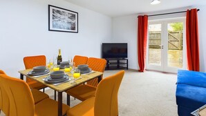 A dining area with a table set for four, a television, and a sliding glass door leading to an outdoor area.