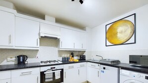 Une cuisine moderne avec des meubles blancs, un plan de travail noir, une cuisinière, un lave-vaisselle et une machine à laver.