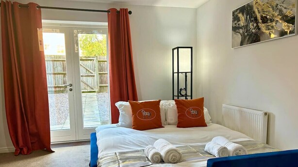 A hotel room with a bed, red curtains, a window, and a painting on the wall.