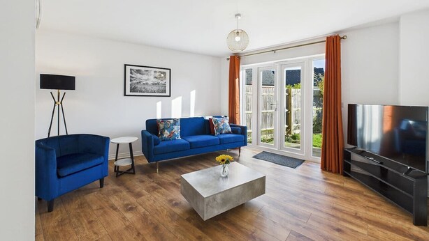 A modern living room with a blue sofa, a coffee table, a flat-screen TV, and a large window with curtains. - *NEW* Prestbury Place | Racecourse | Free Parking (Prestbury)