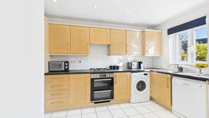 A modern kitchen with wooden cabinets, a built-in oven, a washing machine, and a dishwasher. - *NEW* Prestbury Place | Racecourse | Free Parking (Prestbury)