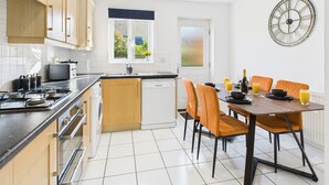 A modern kitchen with a dining area, featuring a dishwasher, stove, and a dining table with chairs. - *NEW* Prestbury Place | Racecourse | Free Parking (Prestbury)