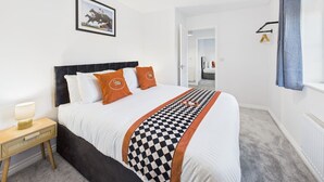 A neatly arranged bedroom with a bed, a bedside table, a hanging light fixture, and a door leading to another room. - *NEW* Prestbury Place | Racecourse | Free Parking (Prestbury)