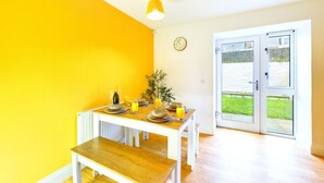 Una habitación luminosa con una mesa de madera preparada para el desayuno, un radiador blanco y vistas a través de puertas de cristal.