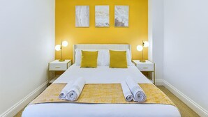 Habitación de hotel con una cama grande, dos lámparas de noche y tres obras de arte colgadas en la pared.