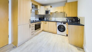 Una cocina compacta con armarios de madera, horno empotrado, microondas y lavadora.