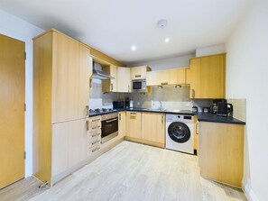 A compact kitchen with wooden cabinets, a built-in oven, microwave, and washing machine.
