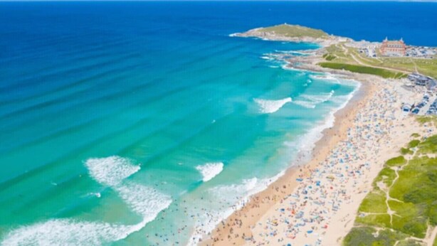 Vista aérea de una playa con mucha gente, aguas azules cristalinas y un edificio al fondo.