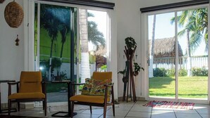 Una habitación amplia con dos sillones amarillos, un gran ventanal corredero que da a un jardín y un alto soporte para plantas.