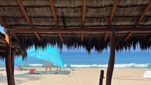 Una playa con una estructura de techo de paja, arena y vista al océano.