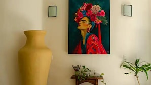 Una habitación con un jarrón grande, un cuadro, una silla, una mesita con plantas y una planta en maceta.