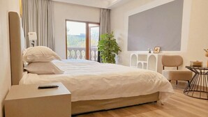 Habitación de hotel con una cama grande, una mesita de noche, una silla, una pequeña mesa y un balcón con vistas.